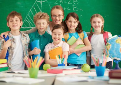 Portrait of cute schoolchildren and their teacher on background of blackboard